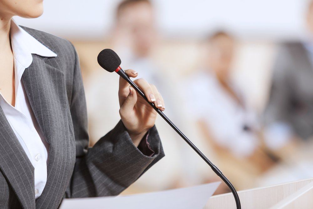 A close-up of a businesswoman in a suit holding a microphone | Jacko Law Group, PC