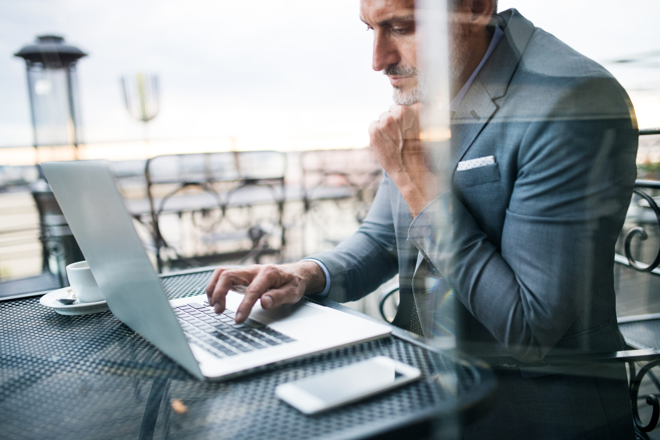 A person in a suit typing on a laptop at an outdoor café | Jacko Law Group, PC