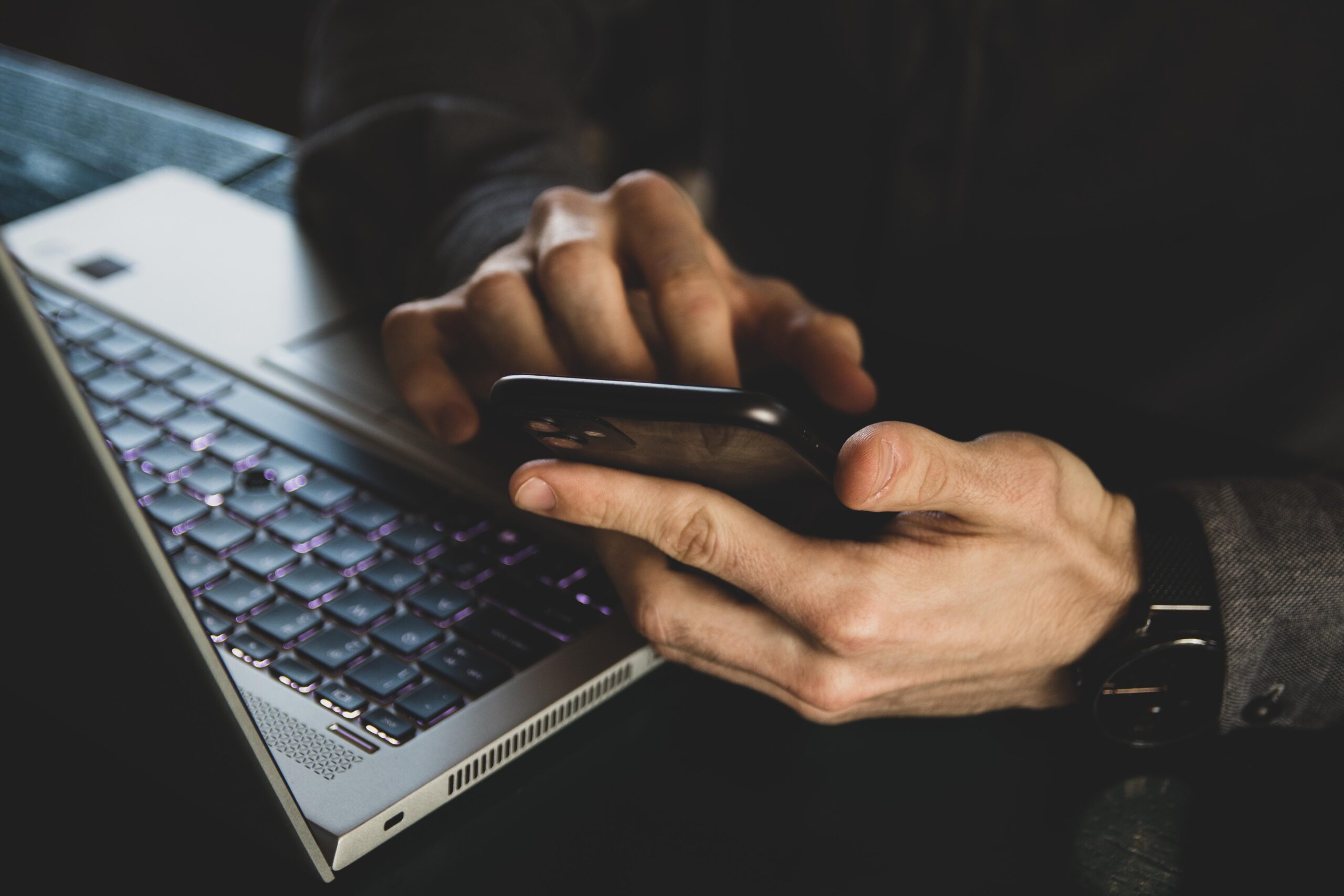 A close-up of hands using a smartphone beside a laptop | Jacko Law Group, PC